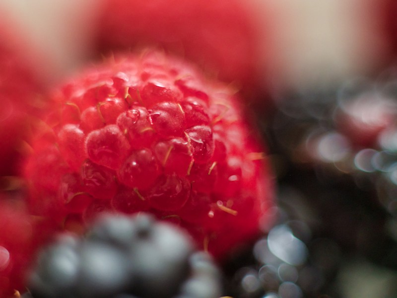 Vibrant red raspberry with blurred blueberries behind